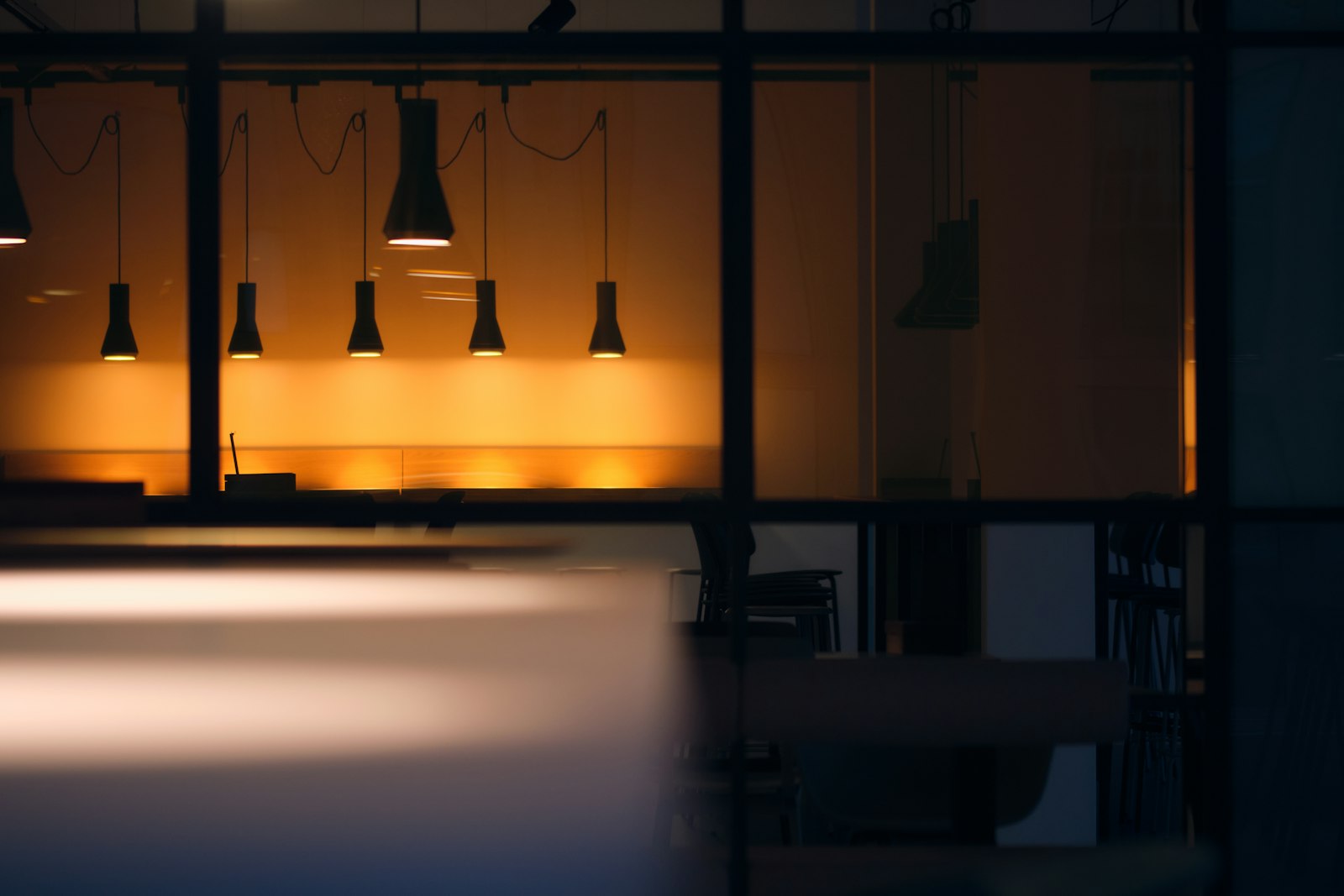 A modern office viewed through a dark glass partition, warm amber light glowing beyond.